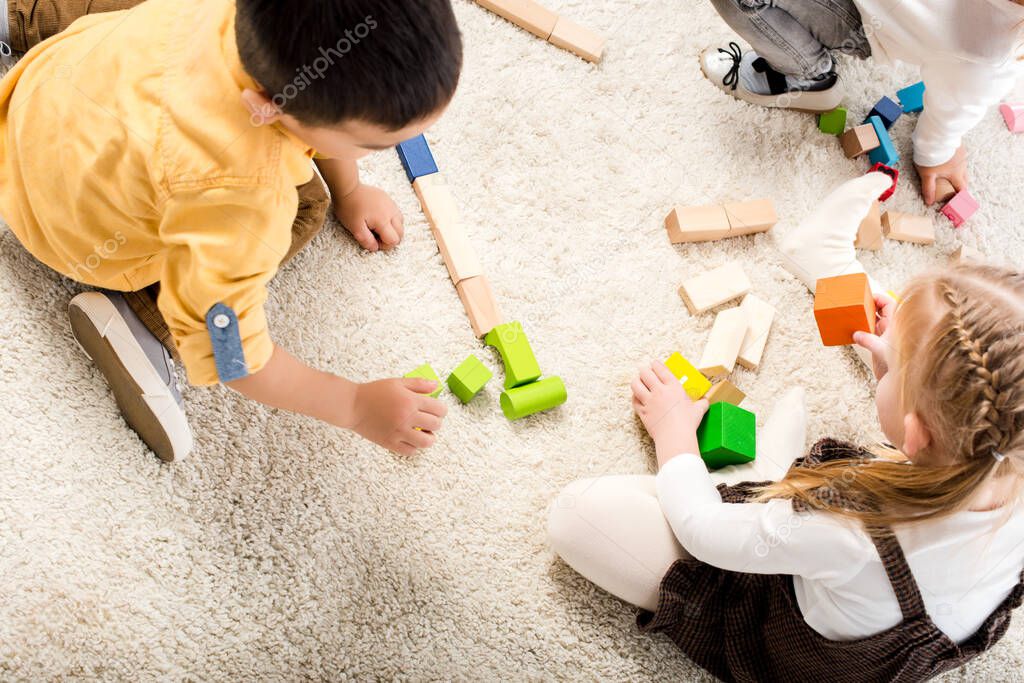 top view of children playing with wooden blocks on carpet