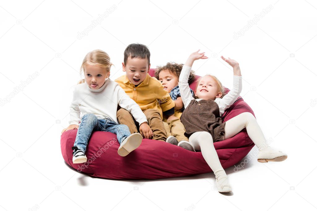 adorable positive multicultural kids playing on red bin bag chair on white