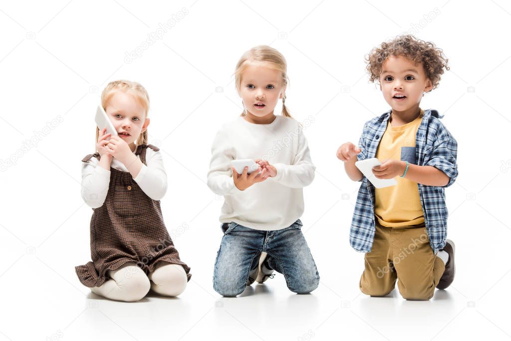 multiethnic children talking smartphones while sitting on white