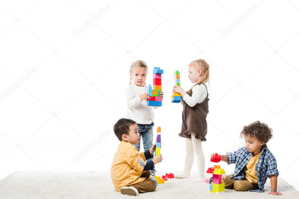 multiethnic children playing with wooden blocks on carpet, isolated on white