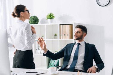 handsome businessman in suit looking and touching secretary in office 