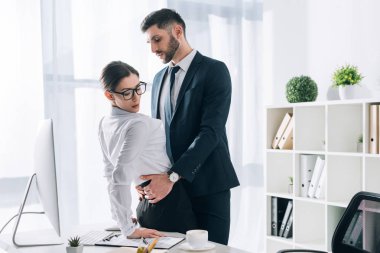 handsome businessman hugging attractive secretary on table in office 