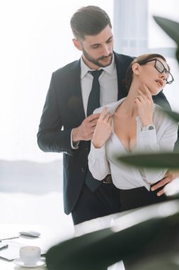 selective focus of businessman hugging sexy secretary with big breast in office 