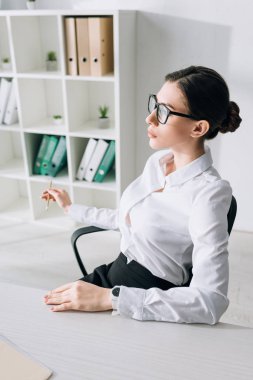 attractive businesswoman sitting at table and looking away in office 