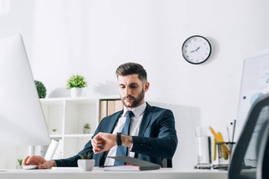 businessman sitting at table and looking at wristwatch in office 