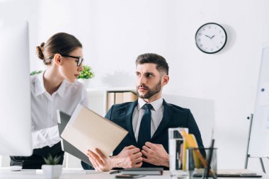 attractive secretary showing folder to handsome businessman in office 