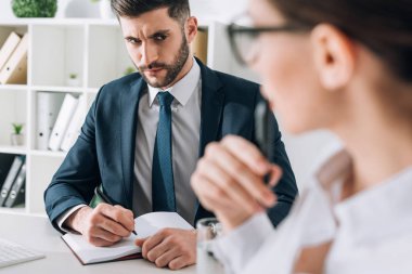 selective focus of businessman sitting at table and looking at secretary in office 
