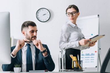 handsome businessman sitting at table and looking at secretary in office 