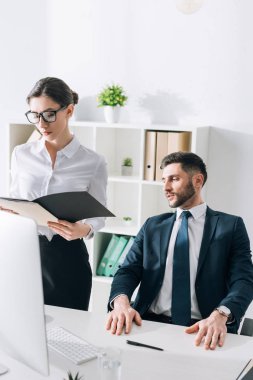 businessman sitting at table and looking at secretary in office 