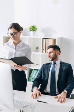 businessman sitting at table and looking at secretary in office 