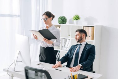 businessman sitting at table and looking at secretary in office 