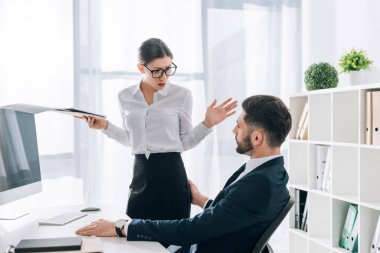 businessman touching butt of shocked secretary with folder in office 