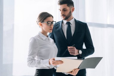 handsome businessman in suit looking at secretary with folder in office 
