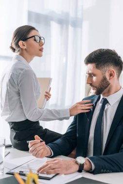 attractive secretary sitting on table and touching businessman in office 