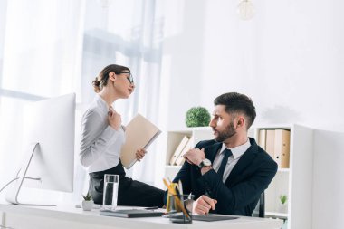 attractive secretary sitting on table and seducing businessman in office 