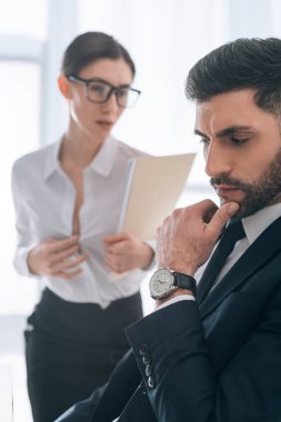 selective focus of pensive businessman and secretary with big bust on background