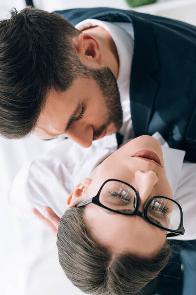 overhead view of businessman in suit kissing secretary in office 