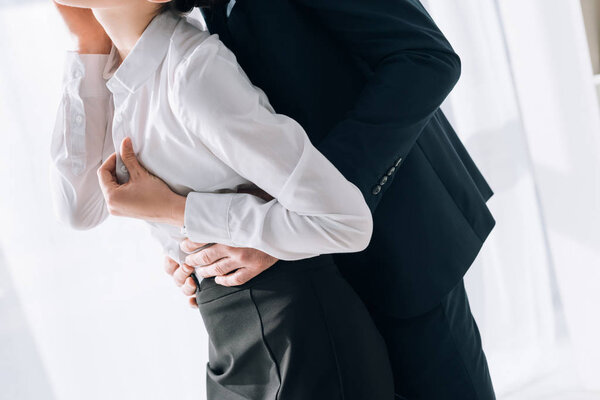 cropped view of businessman in suit hugging secretary in office 