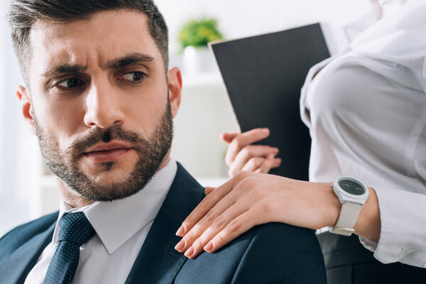 cropped view of secretary with folder touching shoulder of businessman in office 