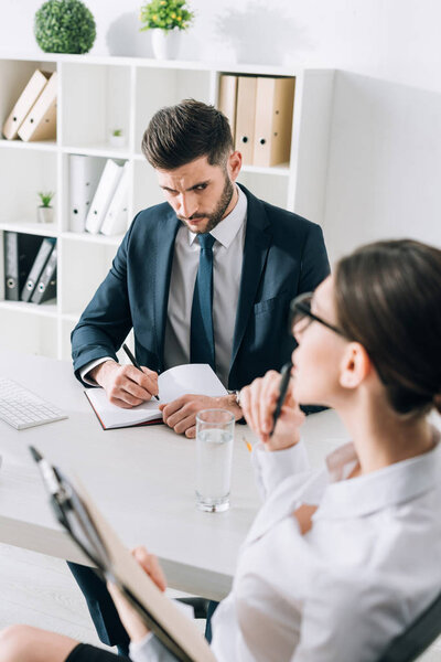 selective focus of businessman sitting at table and looking at secretary in office 