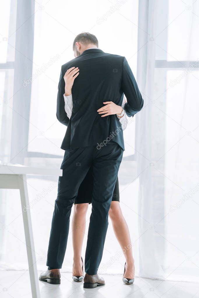 back view of businessman in suit hugging secretary in office 