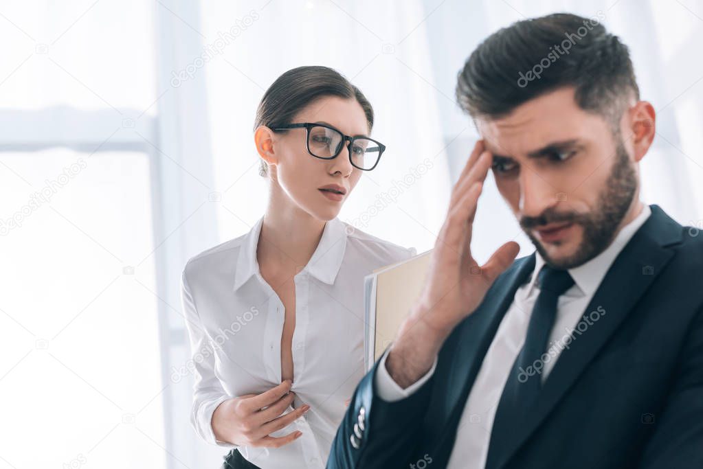 selective focus of secretary with big bust seducing scared businessman in office 