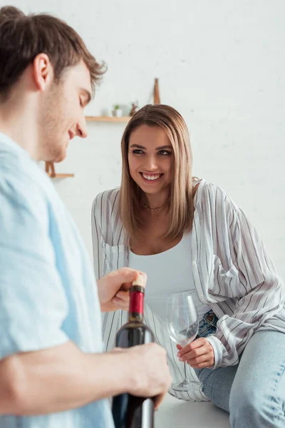 女人看着快乐的男人拿着酒瓶时的选择性焦点 — 图库照片