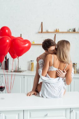 Arka planda, masada oturan seksi bir kadın tişörtsüz erkek arkadaş ve kalp şeklinde balonlar. 