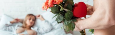 Erkeğin çiçekli ve kalp şeklinde bir hediyeyle baştan çıkarıcı bir kadının yanında çekilmiş panoramik bir fotoğrafı. 