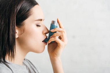 Side view of attractive girl using asthmatic inhaler on white background clipart