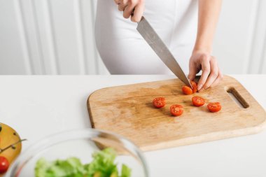 Mutfak masasında taze salatanın yanında vişneli domates doğrayan bir kız görüntüsü.