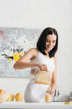 Attractive fit sportswoman pouring smoothie in glass on kitchen table
