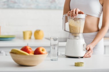 Cropped view of sportswoman preparing smoothie near measuring tape on kitchen table