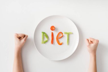 Top view of female fists with diet lettering from vegetable slices on white background