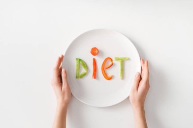 Top view of woman holding plate with diet lettering from vegetable slices on white background