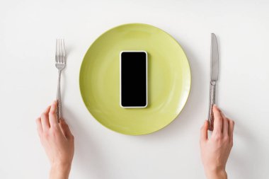 Top view of female hands with cutlery and smartphone on plate on white background