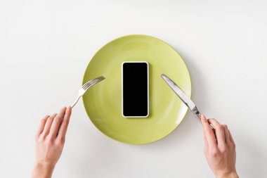 Top view of woman holding cutlery near smartphone on plate on white background