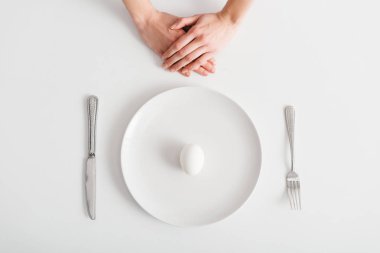 Top view of female hands near egg on plate and cutlery on white background
