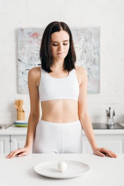 Pensive sportswoman looking at egg on kitchen table