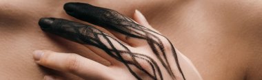 Panoramic shot of nude woman with black painted hand touching chest 