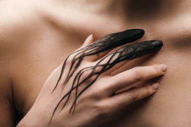 Cropped view of nude woman with black painted hand touching chest 