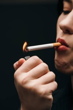 Cropped view of woman lighting cigarette with lighter isolated on black  clipart