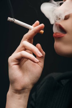 Cropped view of woman smoking cigarette isolated on black 