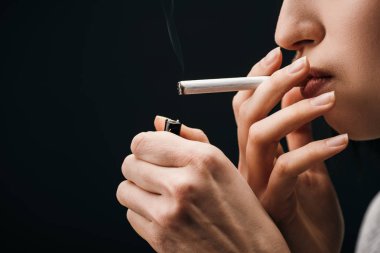 Side view of young woman lighting cigarette with lighter isolated on black 