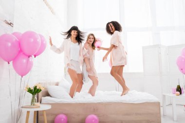 emotional multiethnic girlfriends jumping on bed with pink balloons  clipart