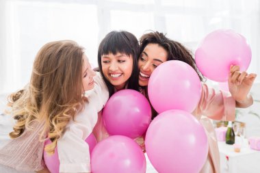 emotional multicultural girls having fun with pink balloons on pajama party clipart