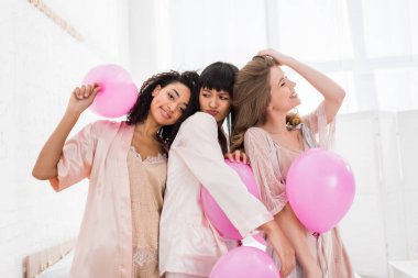 çekici çok kültürlü kızlar yatak odasında pembe balonlarla eğleniyorlar.