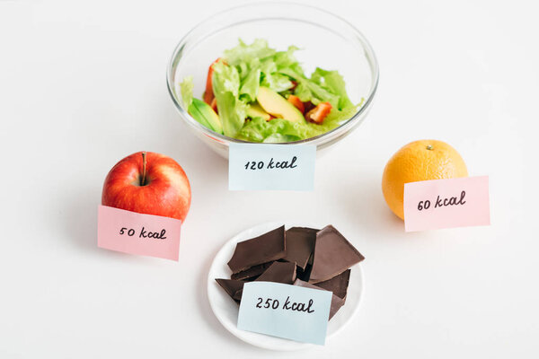 Fresh fruits, chocolate and salad with calories on cards on white background, calorie counting diet