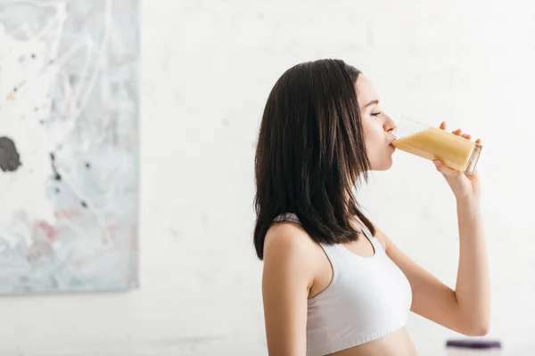 キッチンでスムージーを飲む魅力的なスポーツ女性の側面図 — ストック写真