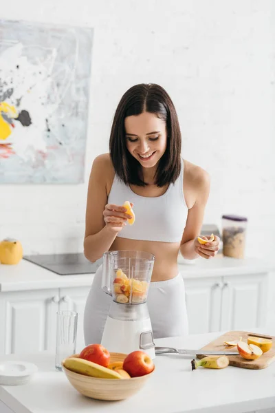 Sorrindo Sportswoman Ajuste Adicionando Frutas Frescas Liquidificador Mesa Cozinha — Fotografia de Stock